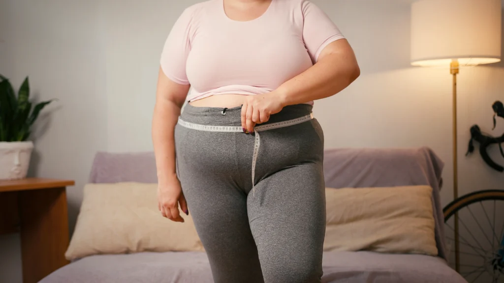 A obese woman measuring her waist using a inch tape